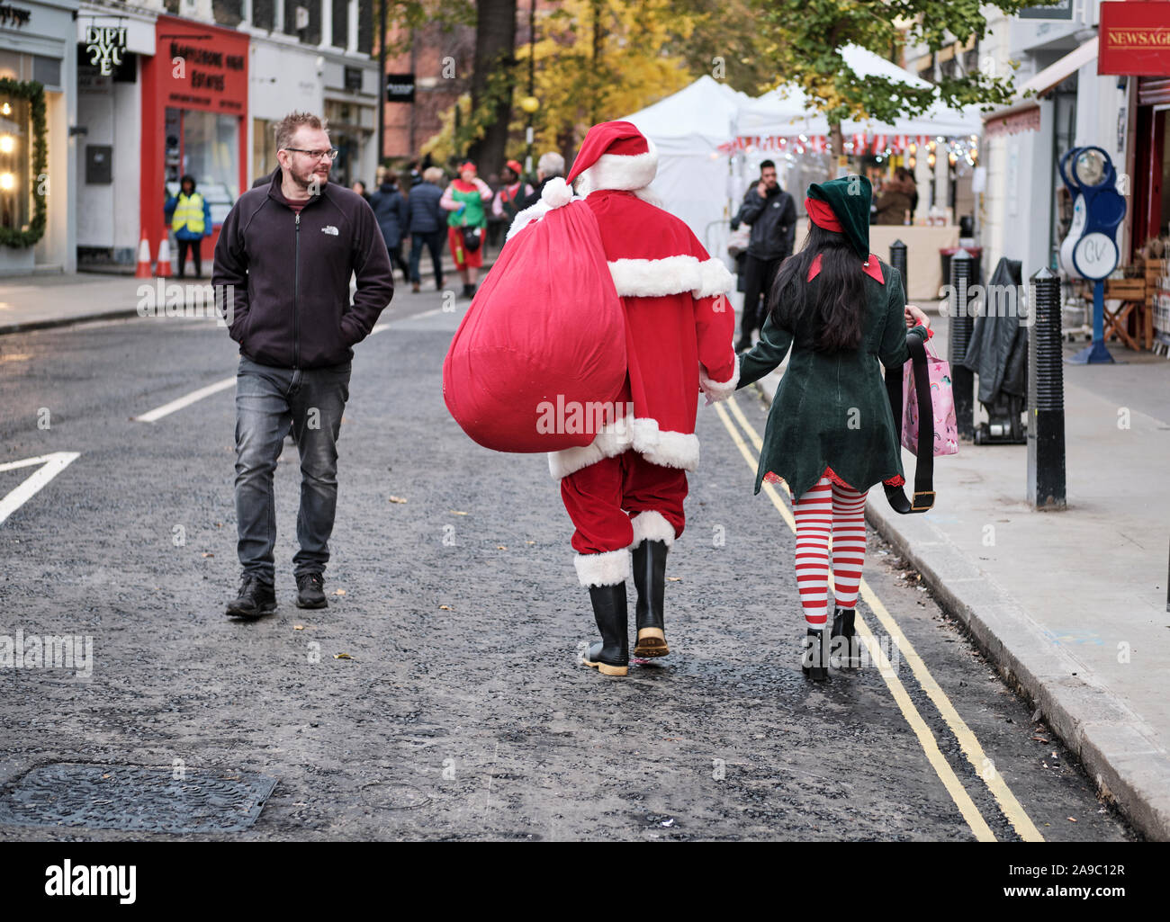 Father Christmas and a female Elf walking away hand in hand getting look from passer-by on London Street Stock Photo