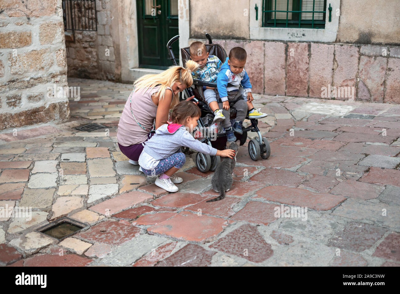 Montenegro, Sep 22, 2019: Mother and baby brothers watching little girl while playing with pussycat on the street in Kotor Old Town Stock Photo