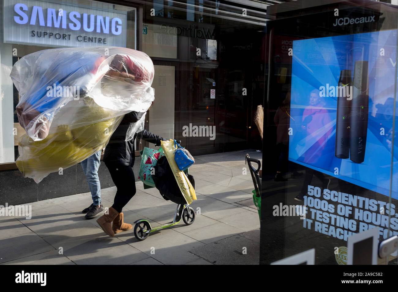 A lady pushes a scooter while carrying inflated party balloons past