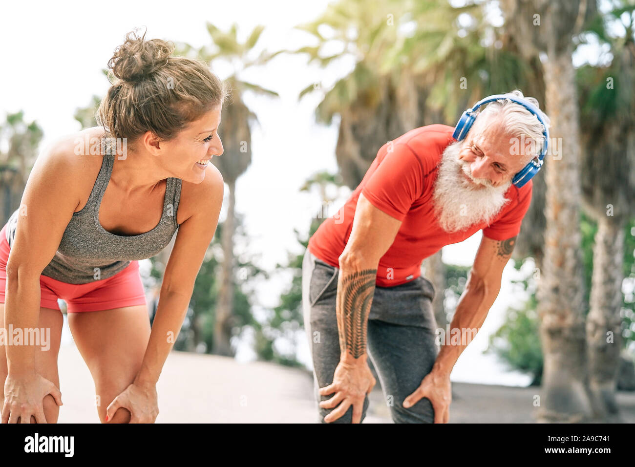 Fit couple of friends having a break after a fast race next the beach at sunset - Sporty people workout outdoor Stock Photo