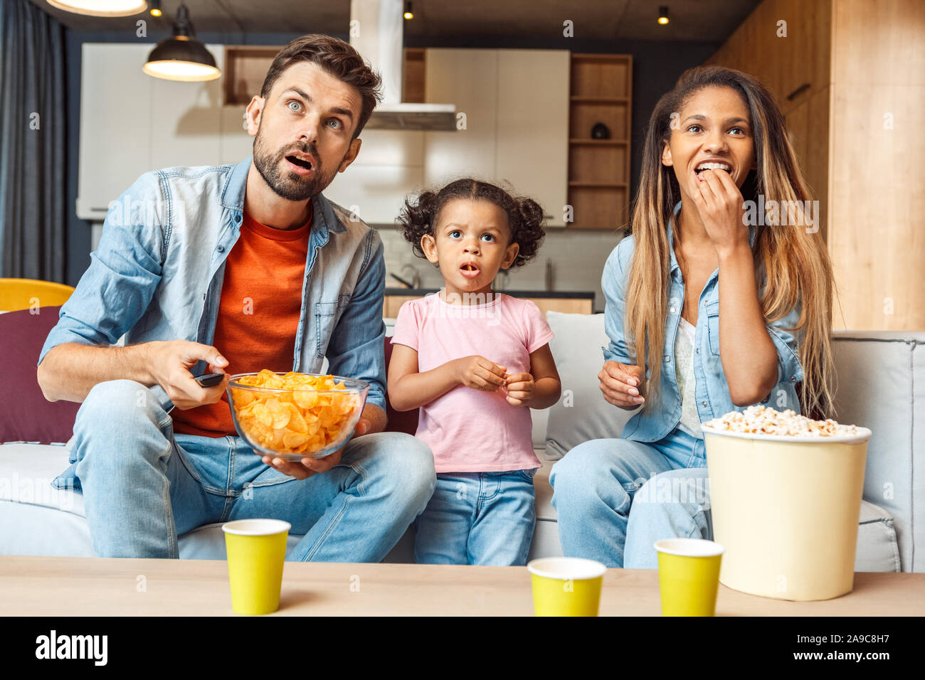 Family watching tv, eating chips and spending day together at home Stock Photo