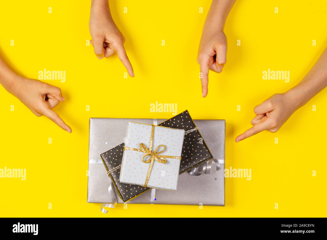 Many hands pointing to wrapped present gift boxes on yellow background. Top view Stock Photo