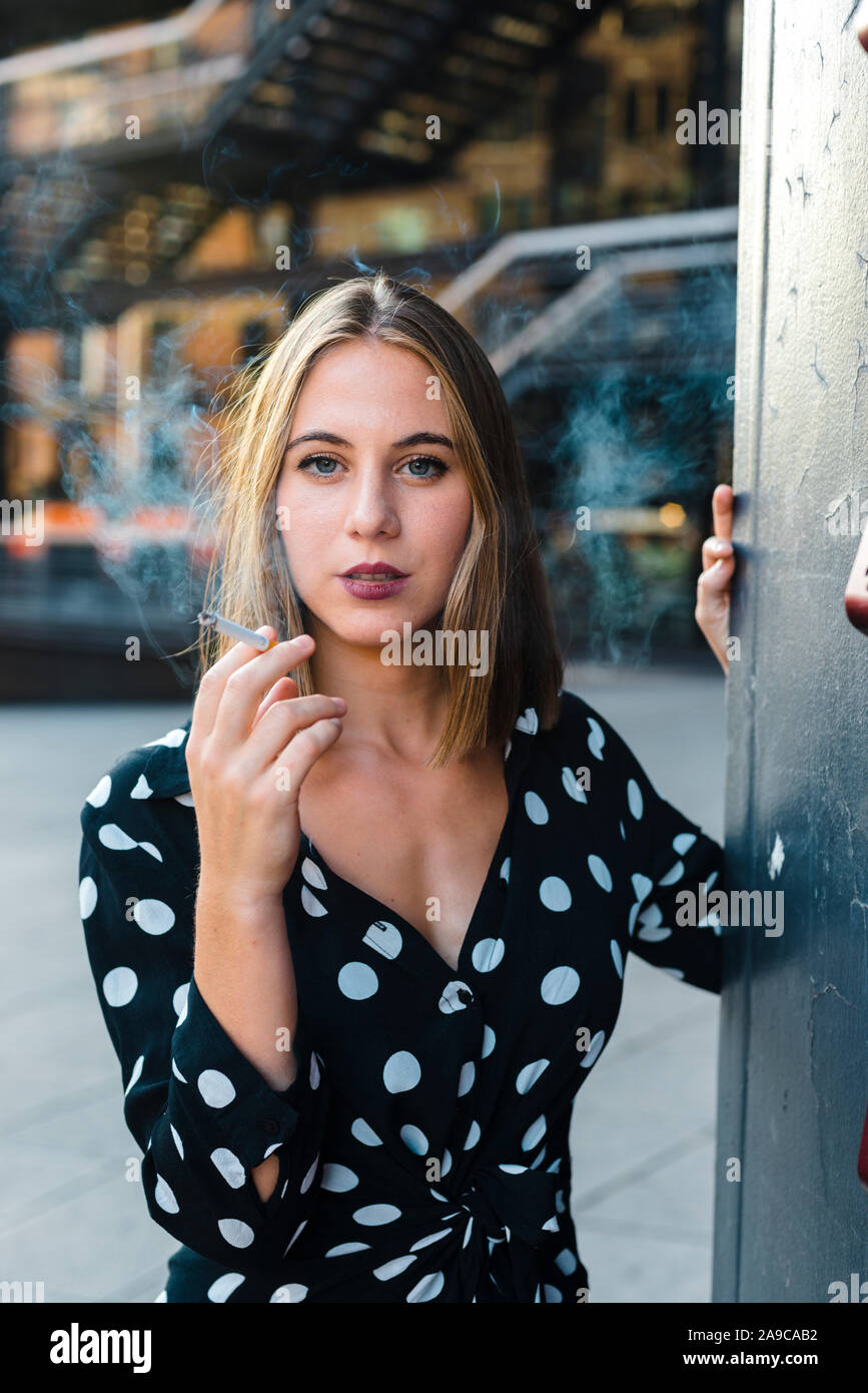 Elegant trendy woman exhaling smoke from cigar looking at camera Stock Photo