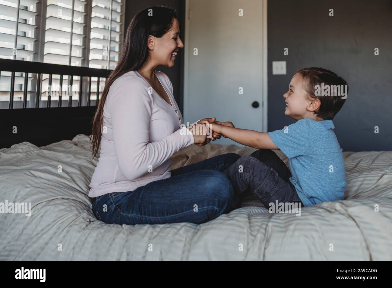 5 yr old boy and mid-30â€™s mom with long dark hair laughing on bed Stock Photo