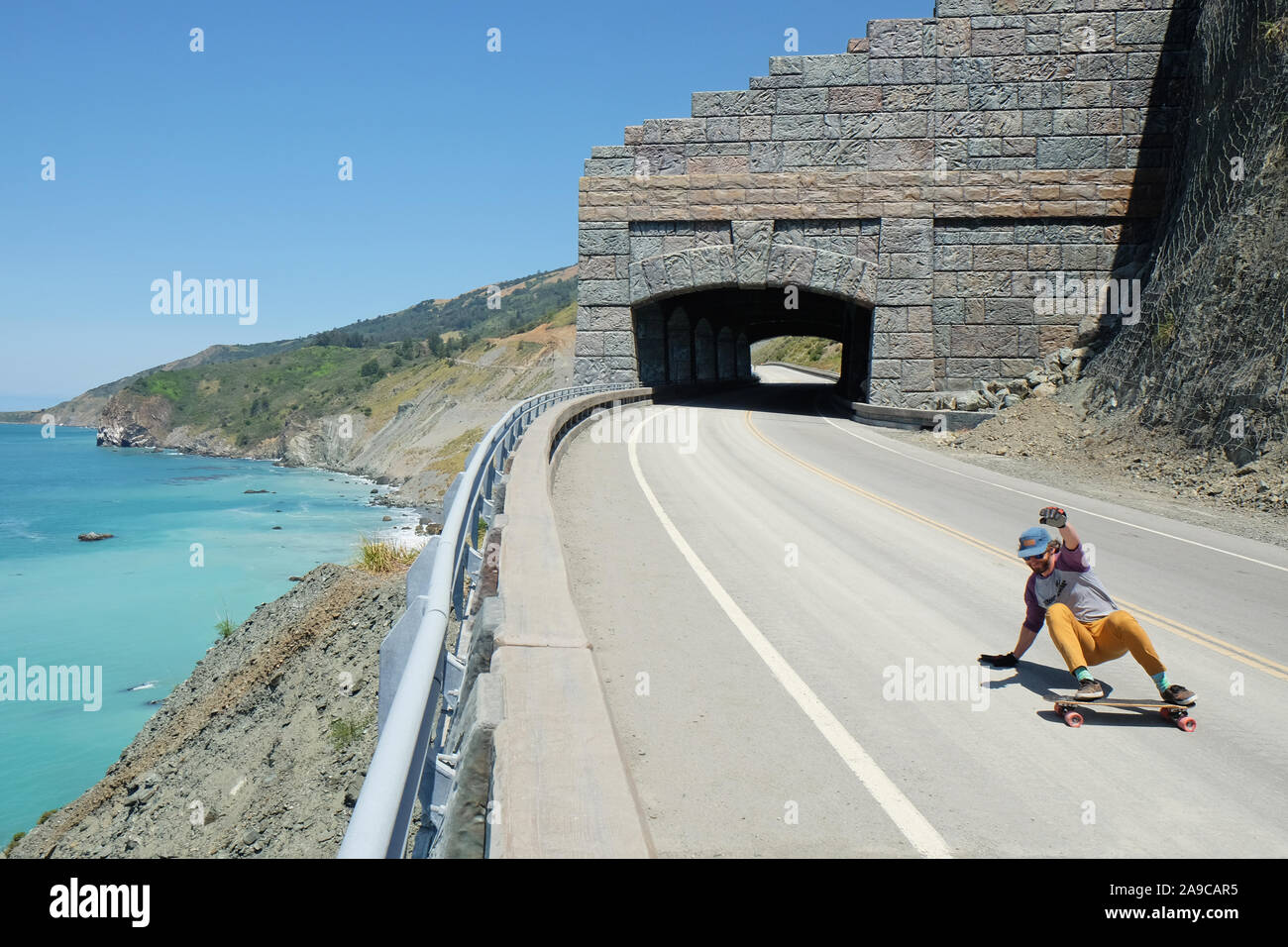 Route One in Big Sur with Man Skateboarding, Ocean and Cliff in Back Stock Photo