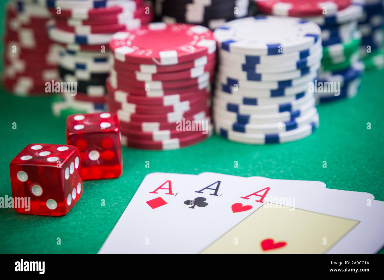 three aces and red cubes with poker chips on green table Stock Photo