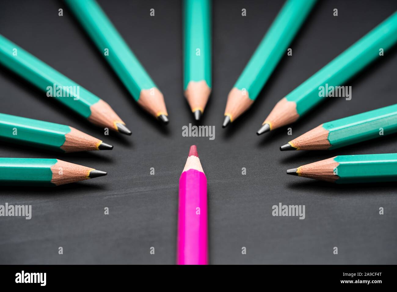 Pink Colored Pencil Surrounded With Green Lead Pencils On Black Chalkboard Stock Photo