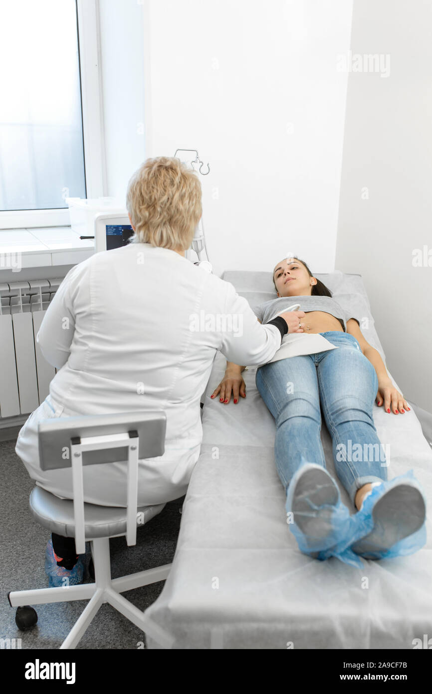 The doctor conducts an ultrasound diagnosis of the patient’s abdomen and internal organs. A girl