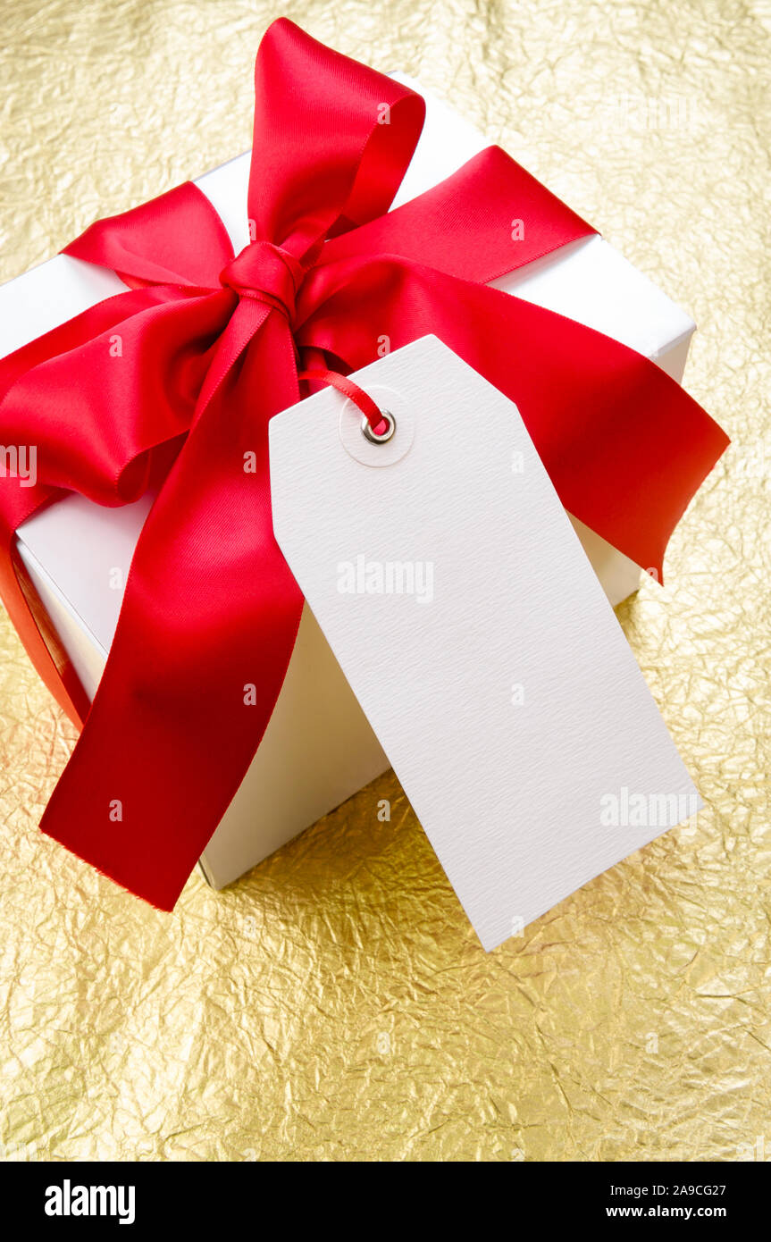 Blank white gift tag hanging from a white box with red satin ribbon on