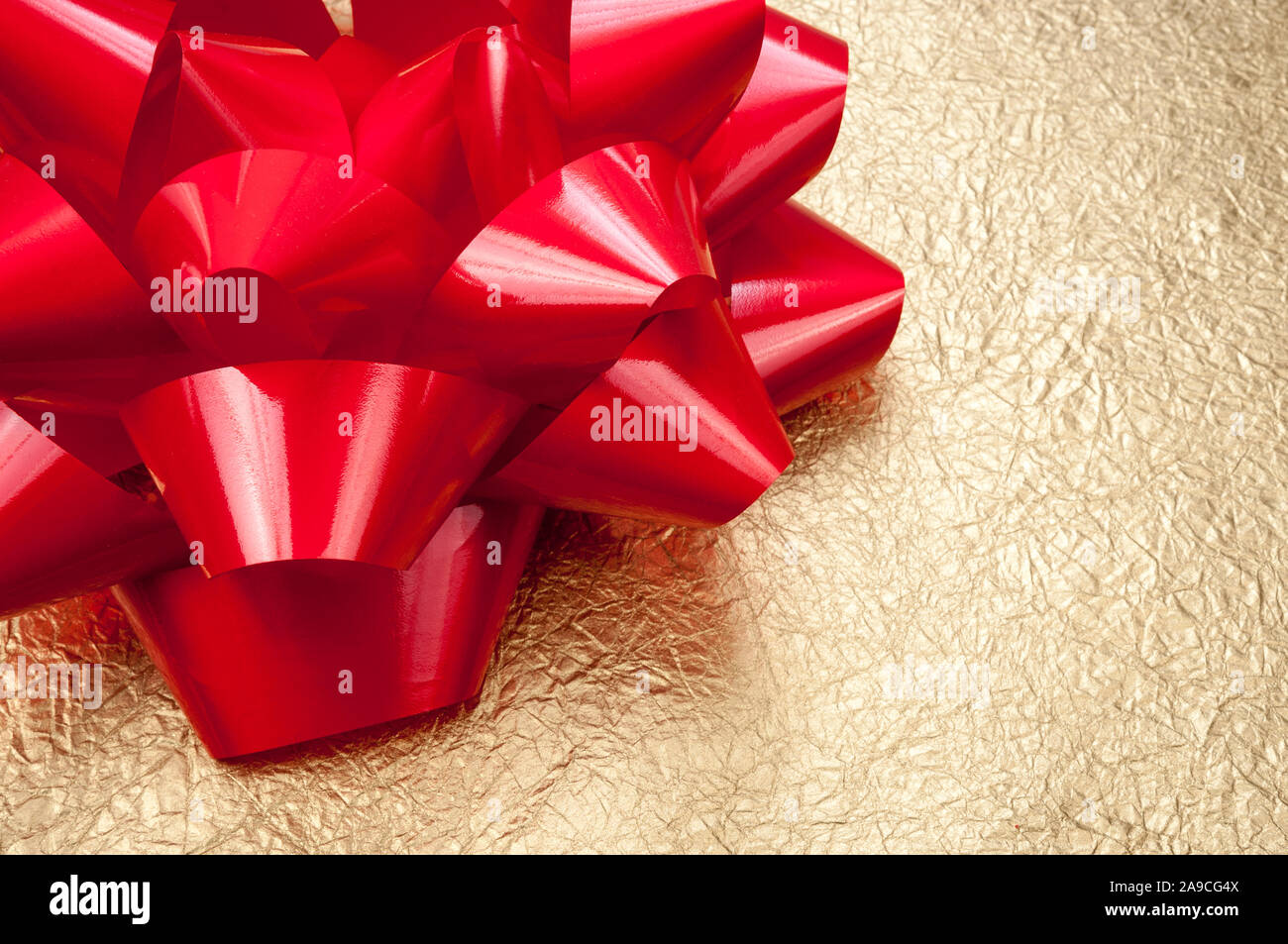 Christmas present wrapped in metallic gold holiday paper topped by a shiny red bow Stock Photo