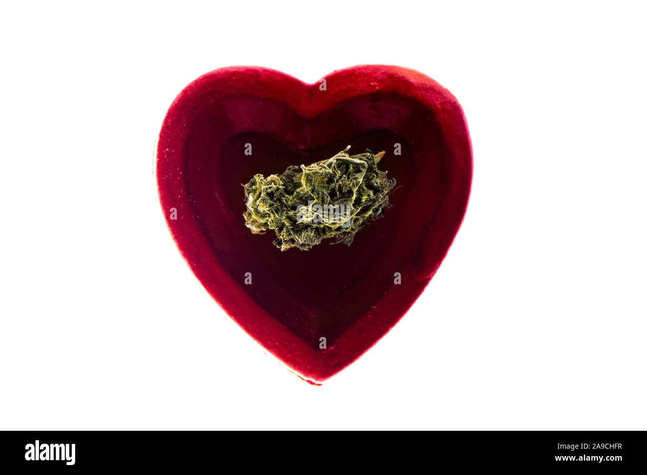 Dried cannabis buds CBD in red heart shape plate on white background. Copy space. Stock Photo