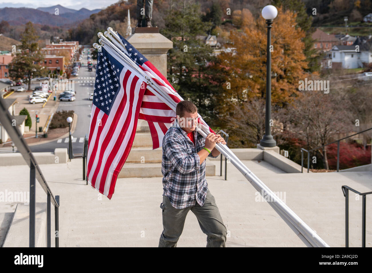 Worker carries American flags used on courthouse lawn, against a backdrop of mountains. Stock Photo