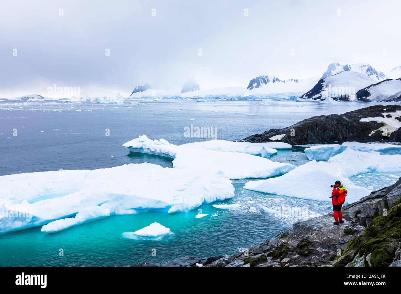Tourist taking photos of amazing frozen landscape in Antarctica with icebergs, snow, mountains and glaciers, beautiful nature in Antarctic Peninsula w Stock Photo