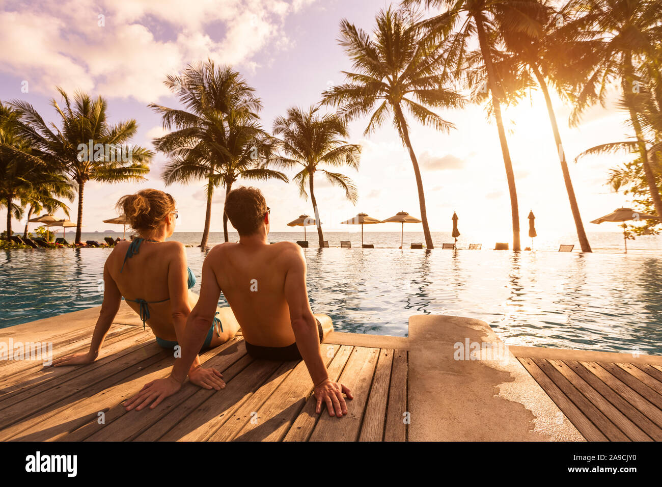 Couple enjoying beach vacation holidays at tropical resort with swimming pool and coconut palm trees near the coast with beautiful landscape at sunset Stock Photo