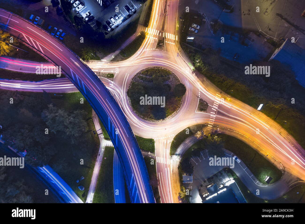 Transportation at night with commuting vehicle traffic creating light trails on the road with motion blur, roundabout and motorway interchange in city Stock Photo