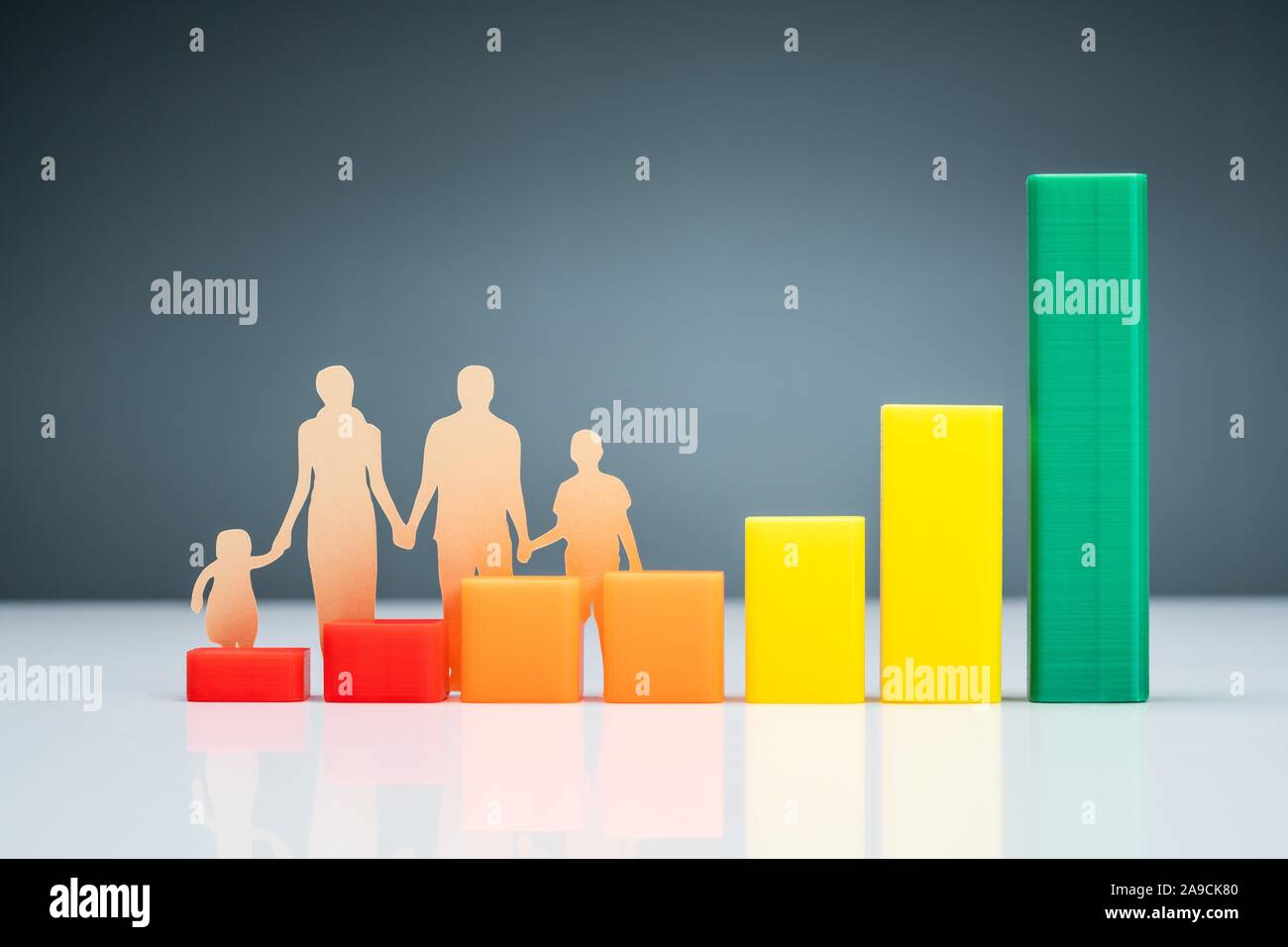 Family Cutout Paper Behind The Colorful Energy Efficiency Rating Chart On Desk Against Gray Background Stock Photo