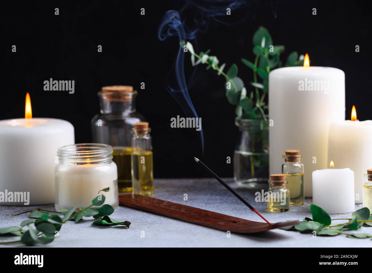 Incense stick with smoke on stone with white candles and essential oils