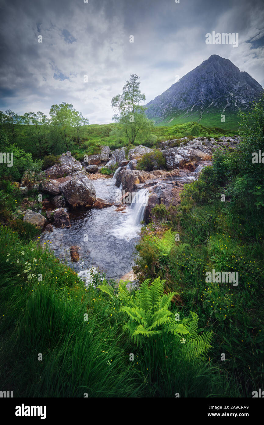 Small waterfall betwwen the grass and a mountain in Glen Etive valley, in Highlands of Scotland. Etive river. Cloudy day. Stock Photo