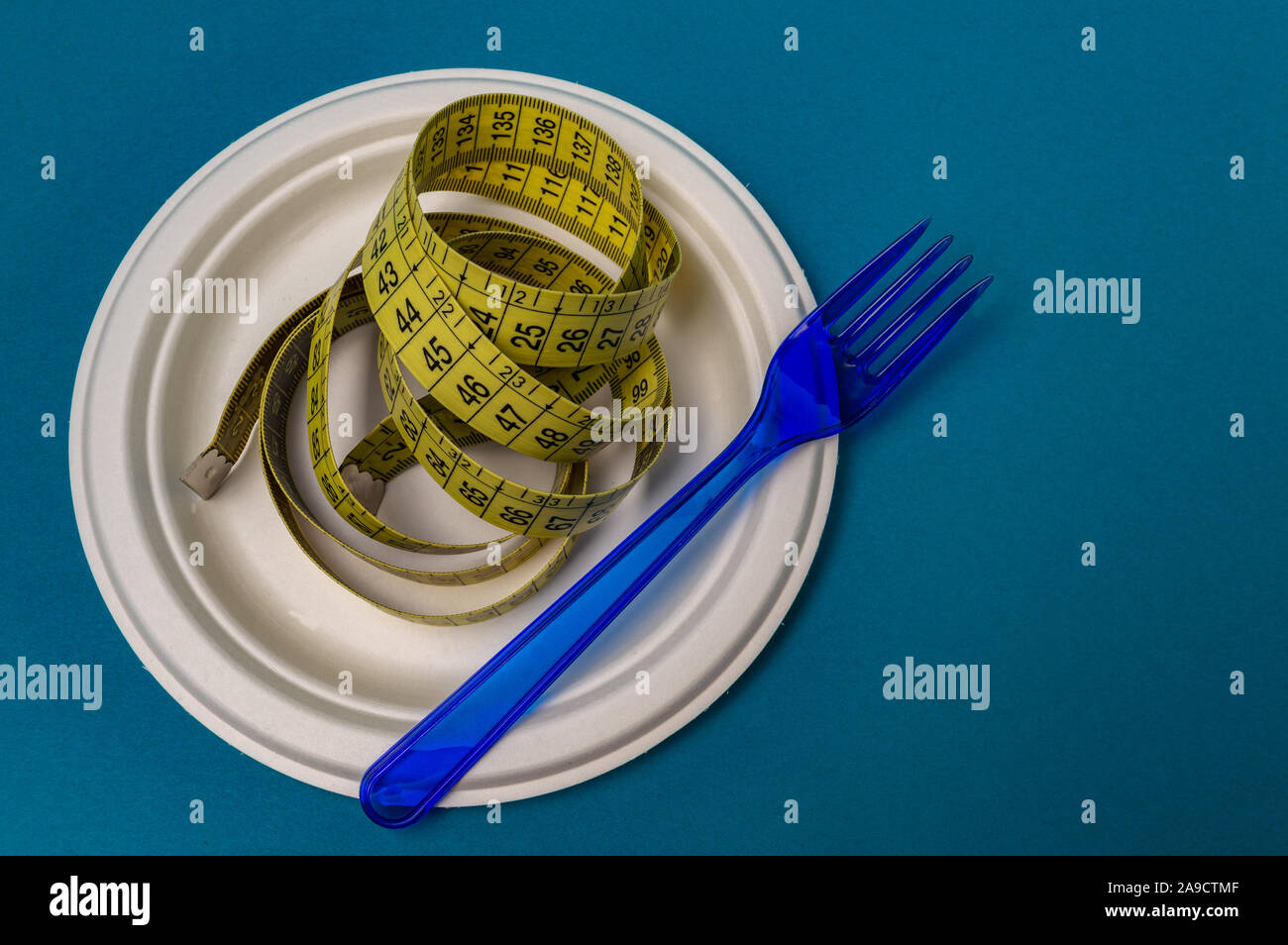 plastic blue fork, plastic plate, measuring tape blue background. closeup Stock Photo