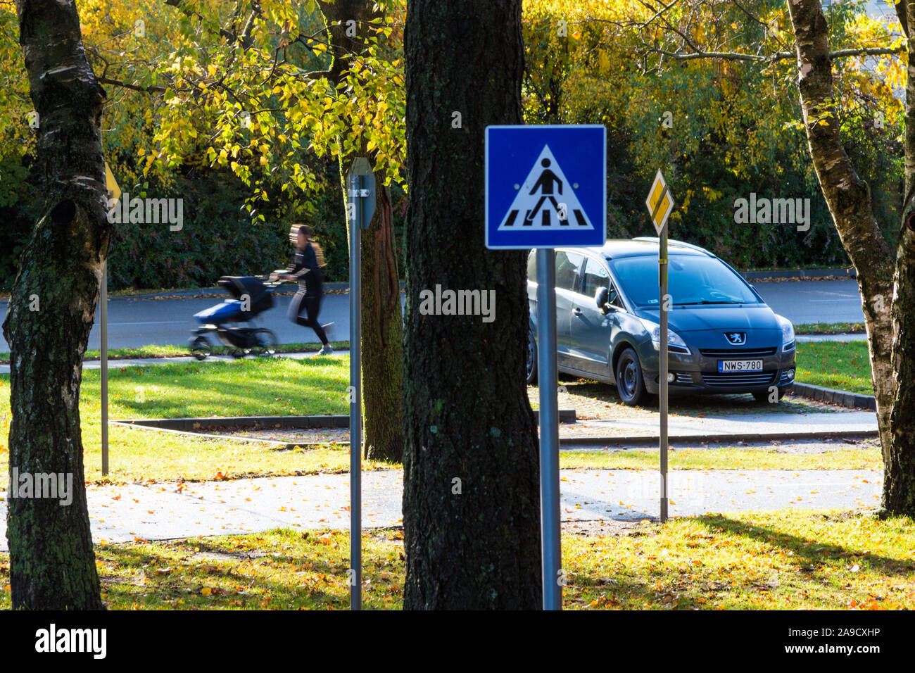 Running jogging young woman pushing pram beside car and traffic signs near traffic training course park, Sopron, Hungary Stock Photo