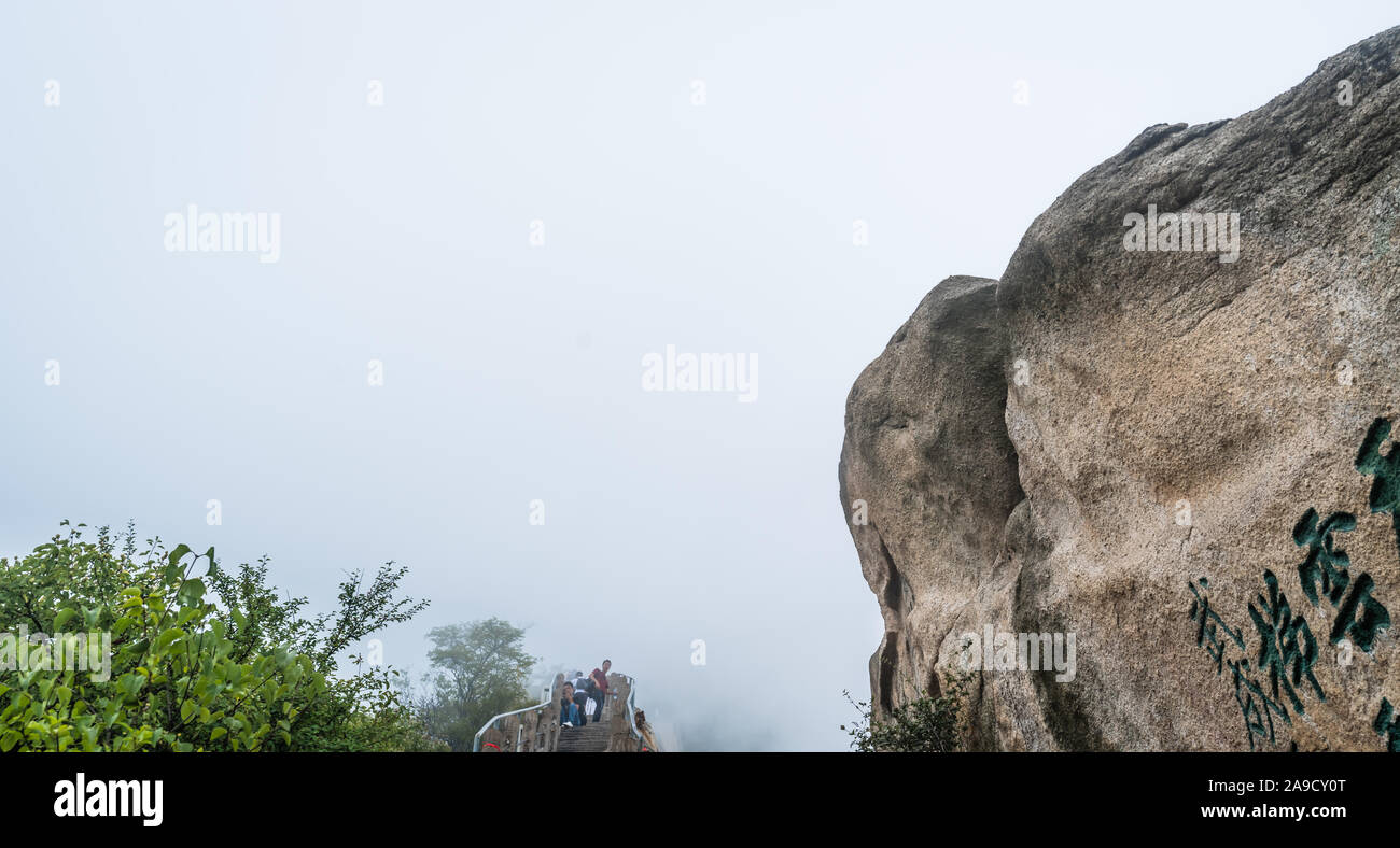 Huashan, China -  August 2019 : Tourists resting on a covered in fog and mist scenic mountain trail to the North and West Peak on Hua shan mountain, X Stock Photo