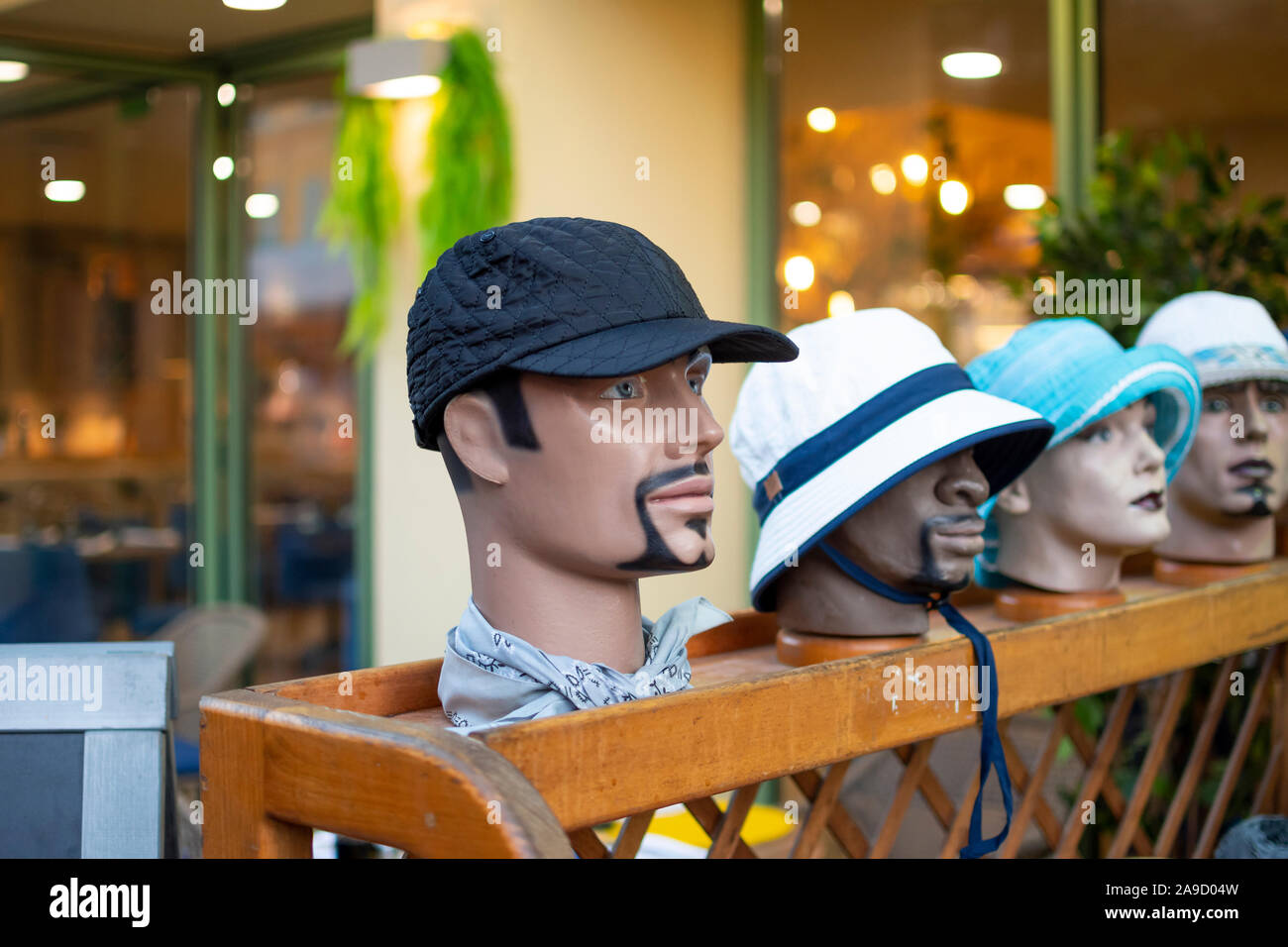 Four mannequin heads of different sexes and race line up outside a store modeling different color hats Stock Photo
