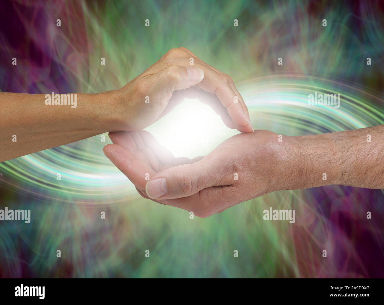 Together our energy is stronger - female hand cupped over a male cupped hand with a bright white orb light between flowing out either side Stock Photo