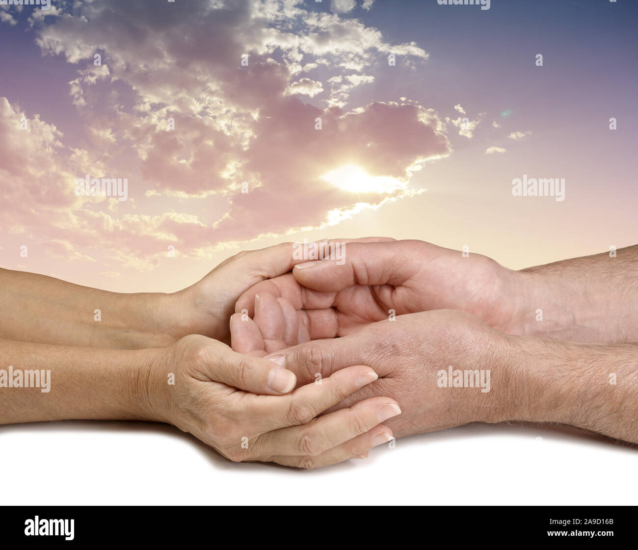 Shedding light on charitable requests - female hands cupped lovingly around male cupped hands against a cloudscape behind and sun shining through Stock Photo