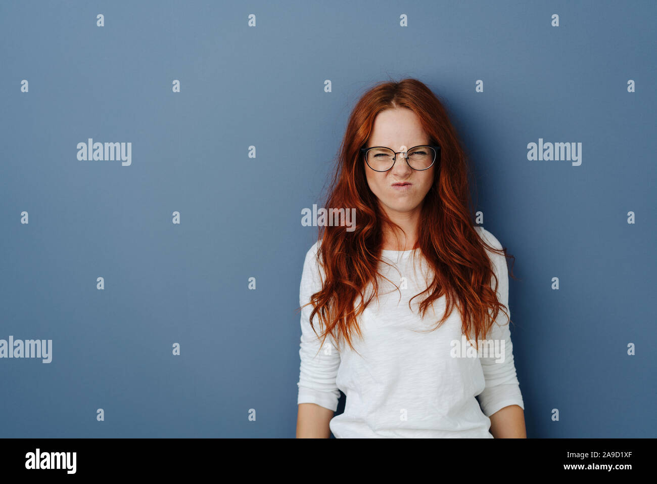 Young woman grimacing in revulsion and aversion screwing up her face and  glaring at the camera over a blue studio background with copy space Stock  Photo - Alamy