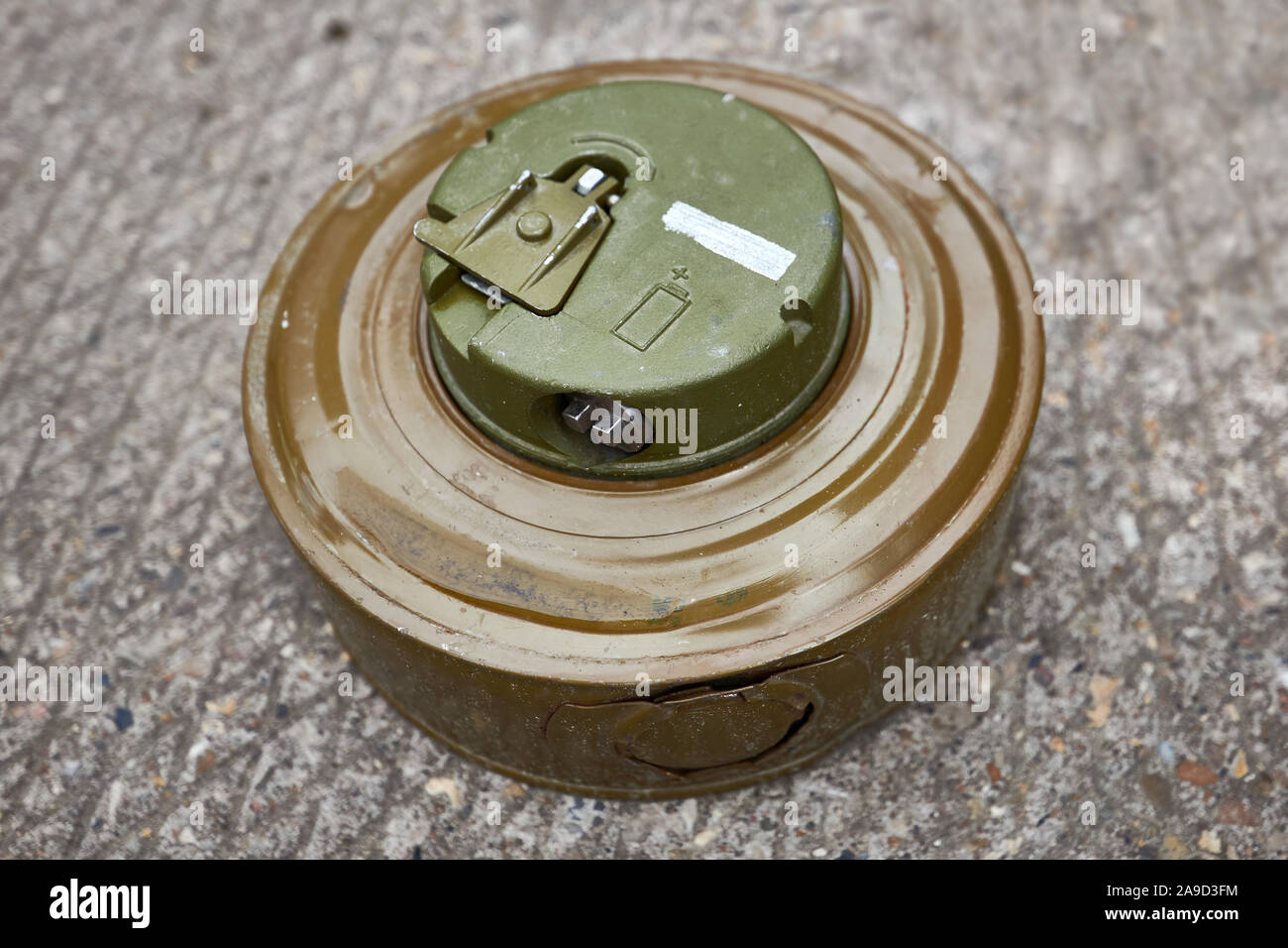 Khaki colour modern anti-tank mine lies on concrete surface. Stock Photo