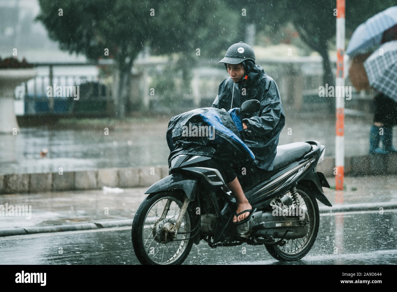 An asian male rides his scooter in the pouring rain in the small little
