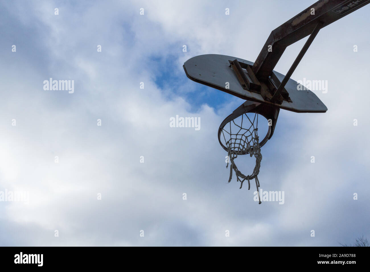 The tattered net of a well used basketball goal against a cloudy sky with a single patch of blue. Stock Photo