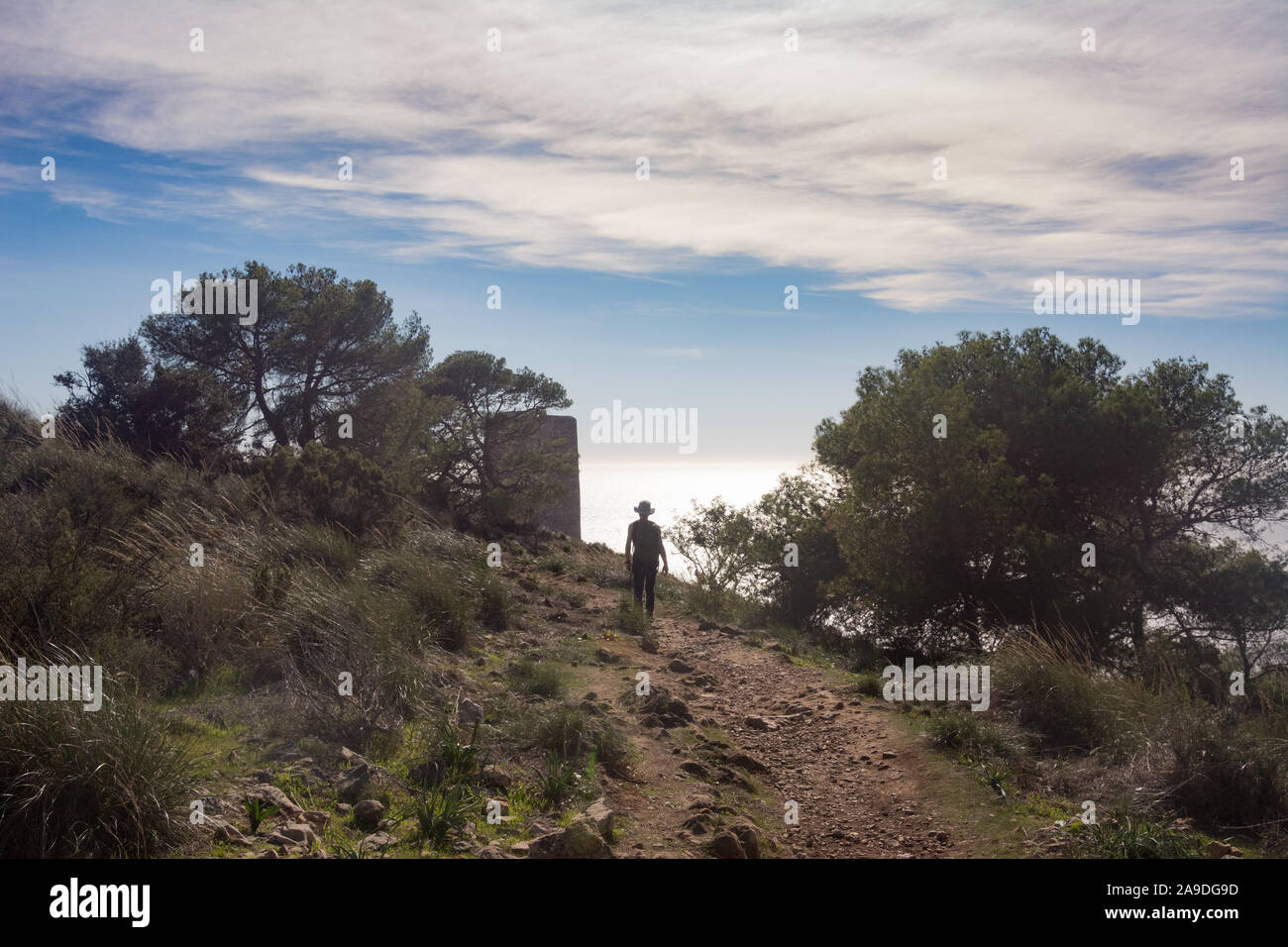 A man hiking the trail on the Cerro Gordo with the watch tower just visible behind the trees. La Herradura, Spain. Stock Photo