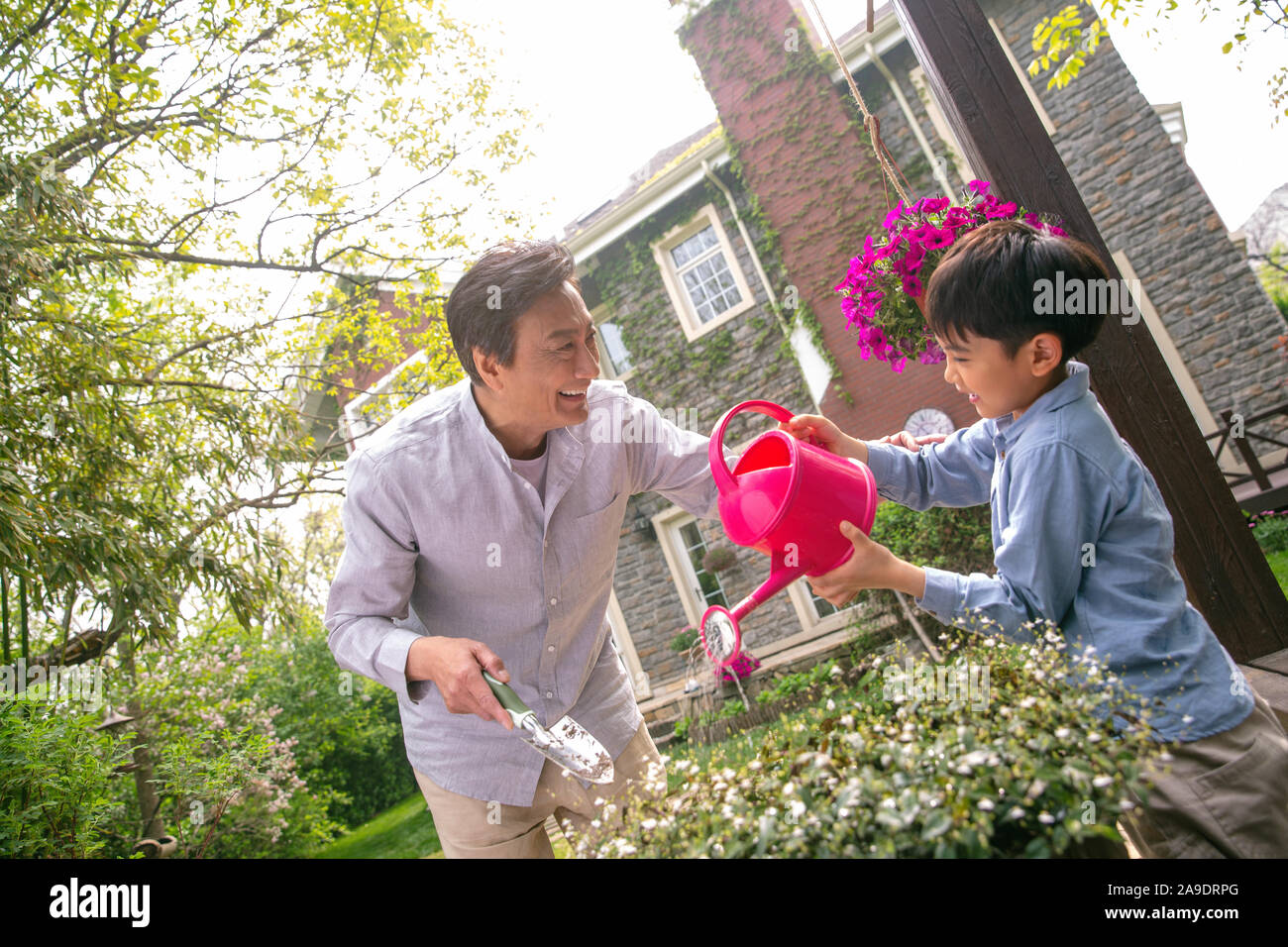 Grandpa and grandson is watering the flowers in the yard Stock Photo