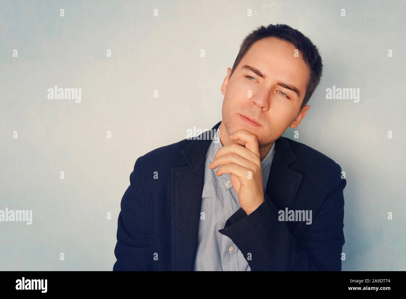 Thoughtful handsome male. A young businessman in a thoughtful pose reflects on business. Thinking through ideas and plans. A grown guy on a blue backg Stock Photo