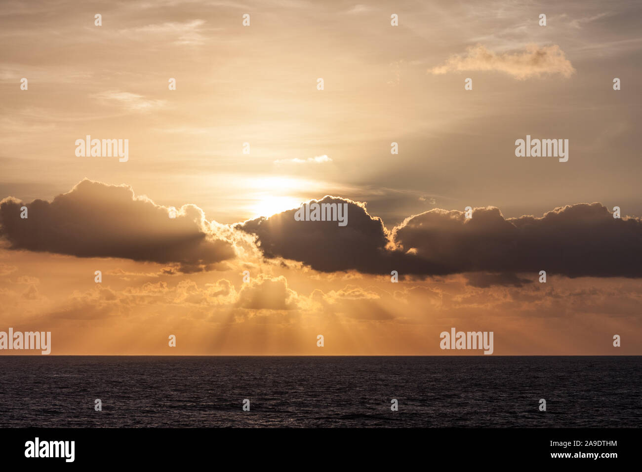 Sunbeams behind clouds at sunset over ocean Stock Photo - Alamy