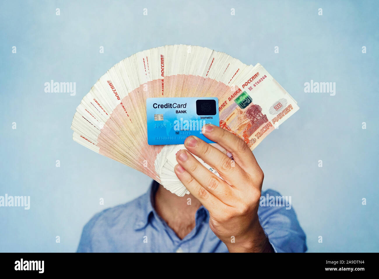 a lot of money and credit card in the hand of a young businessman on a blue background. A stack of banknotes of Russian rubles with a face value of 50 Stock Photo