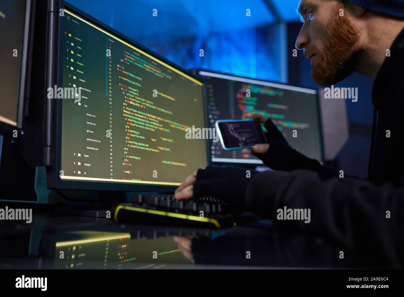 Bearded computer hacker using mobile phone to break the computer system and stealing the information Stock Photo