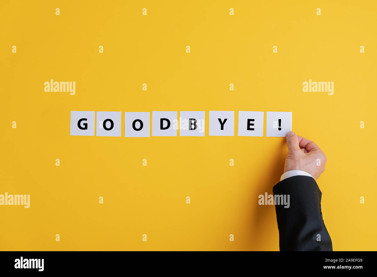Hand of a businessman assembling a Goodbye sign with white post it papers over yellow background. With copy space. Stock Photo