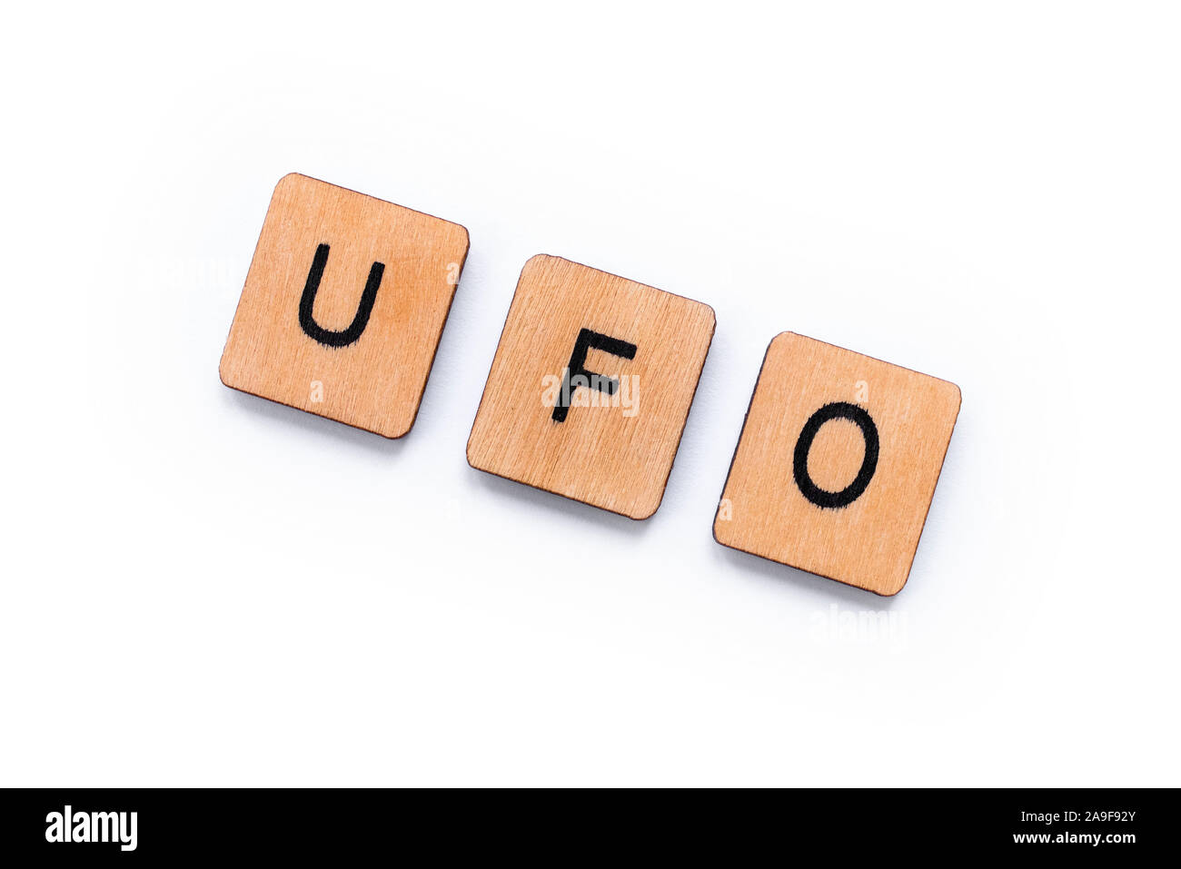 The abbreviation UFO which stands for Unidentified Flying Object, spelt with wooden letter tiles over a white background. Stock Photo