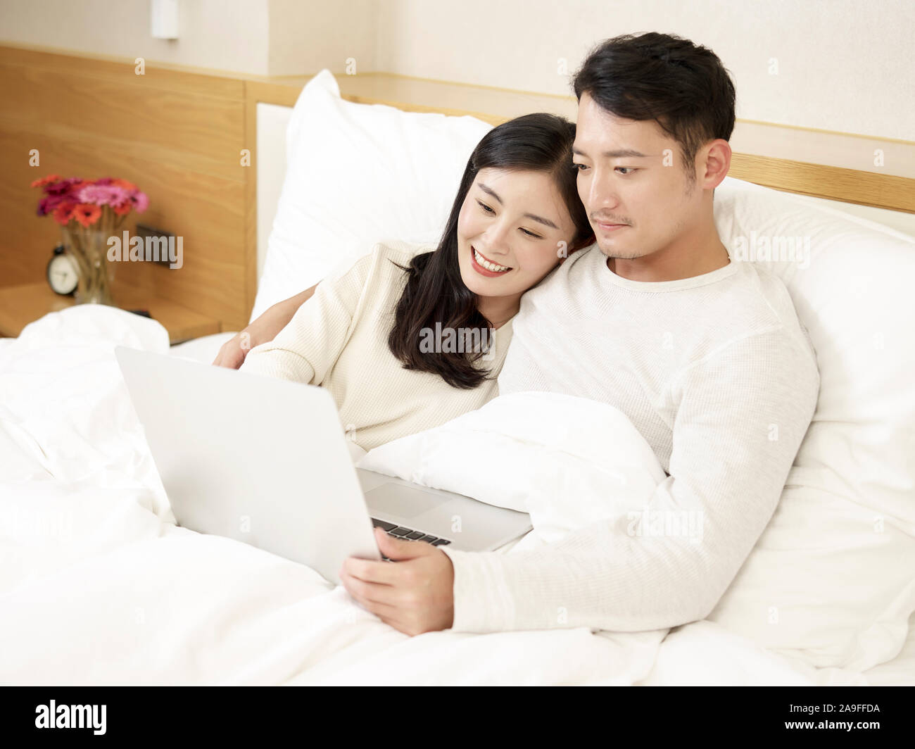 happy young asian couple looking at laptop computer together in bed Stock Photo