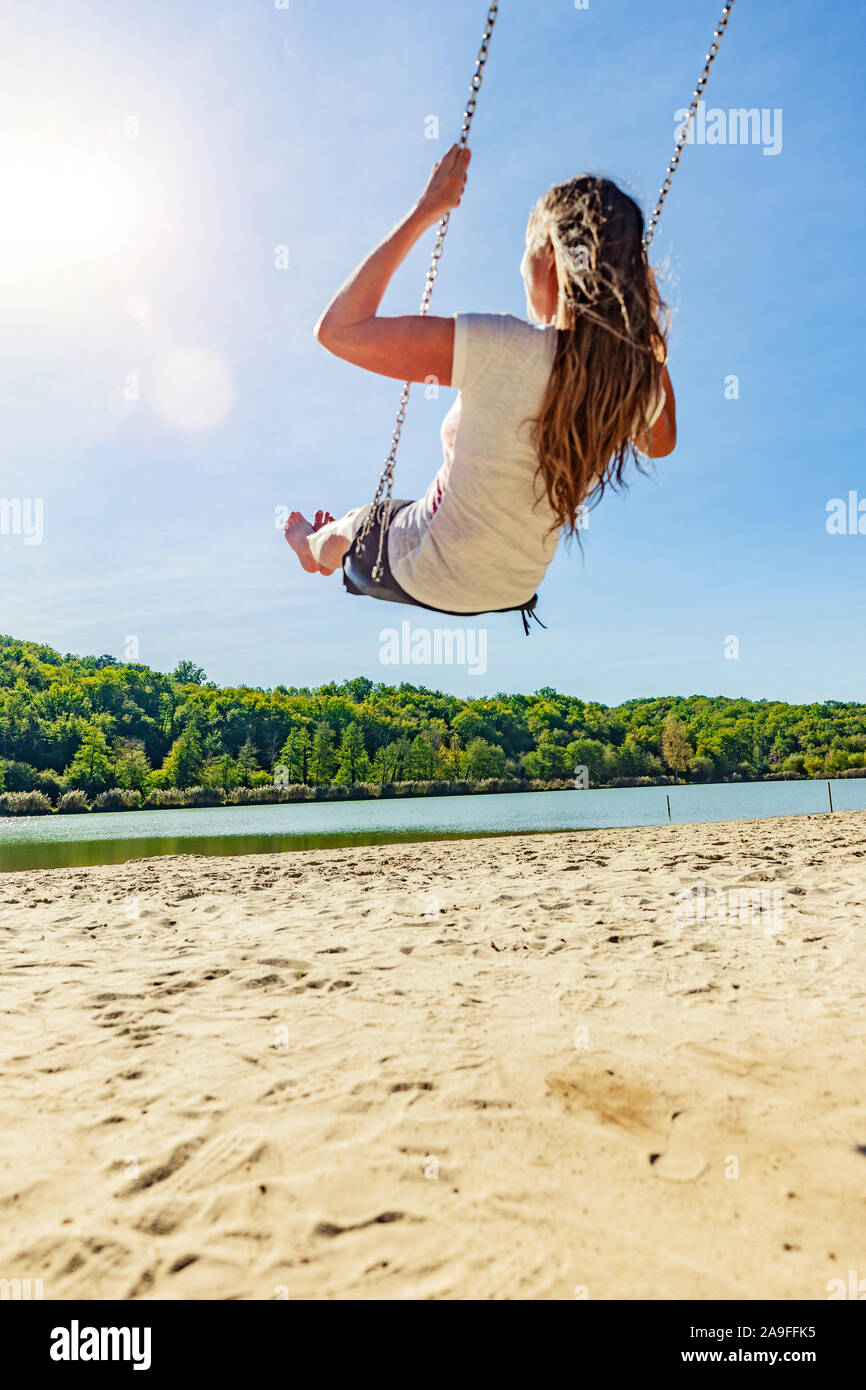 Woman on a swing on a lake with a sandy beach Stock Photo