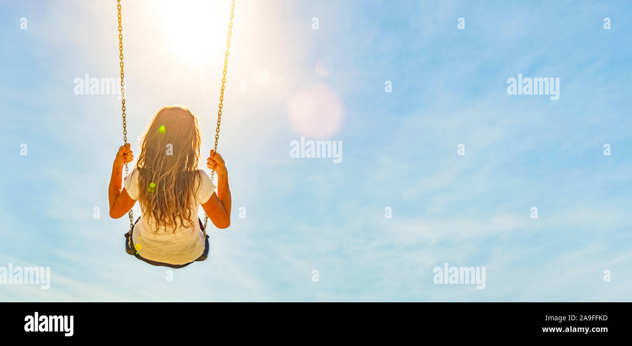 Woman on a swing with blue sky in the back light Stock Photo