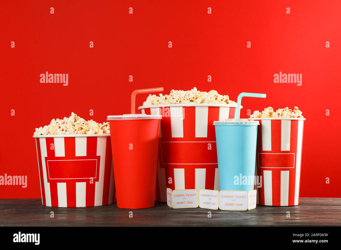 Popcorn buckets, paper cups and tickets against red background, space ...
