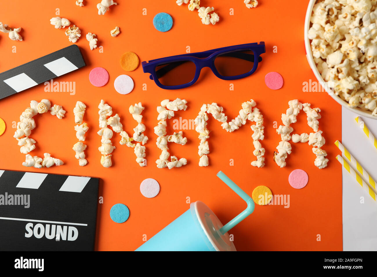 Word cinema laid out from popcorn and movie watch accessories on orange