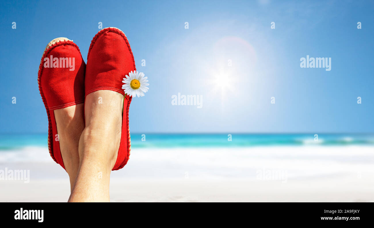 Legs with red cloth shoes and flower in front of beach and sea Stock Photo