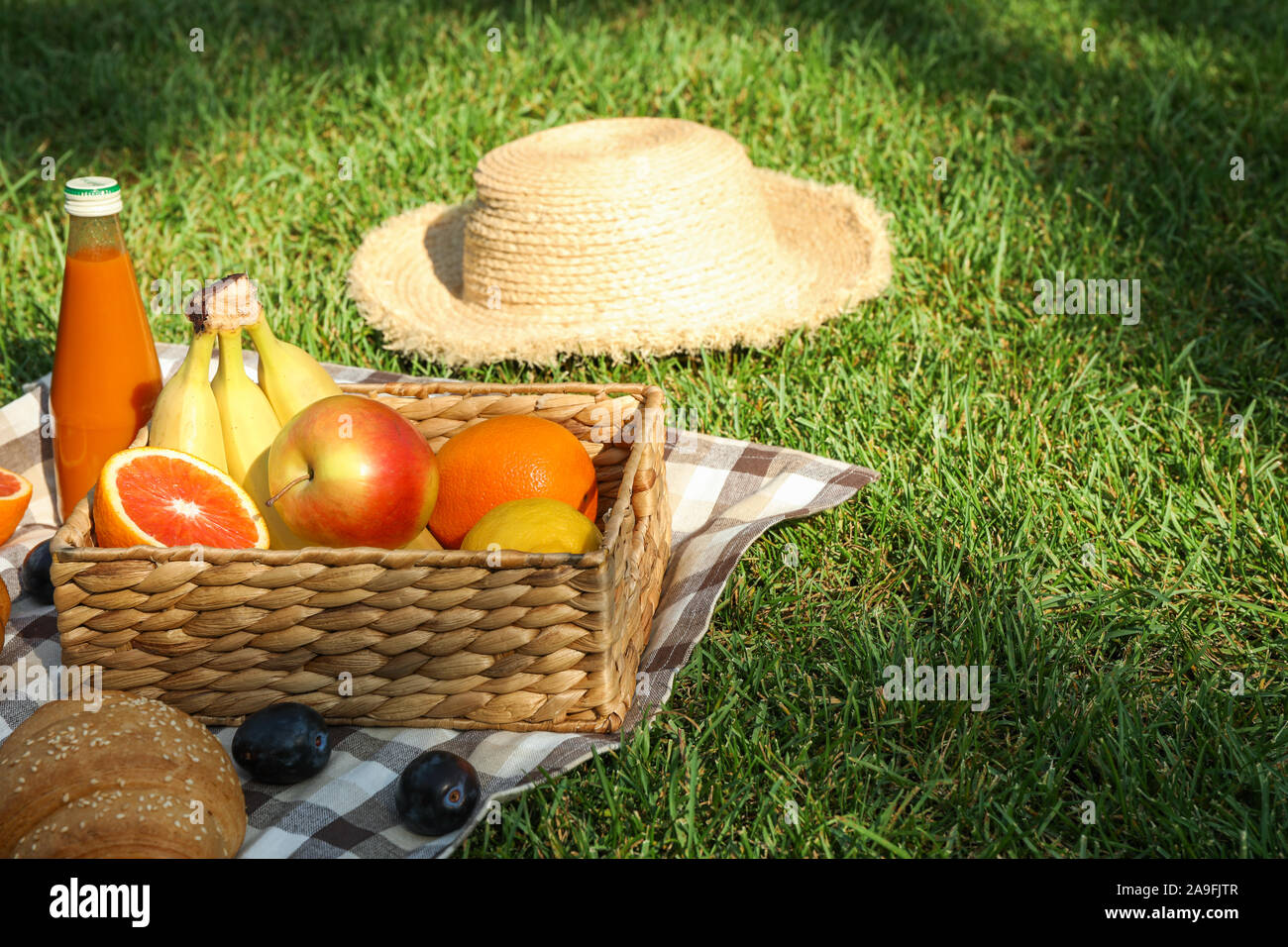 Picnic composition with fruits and straw hat against green grass, space