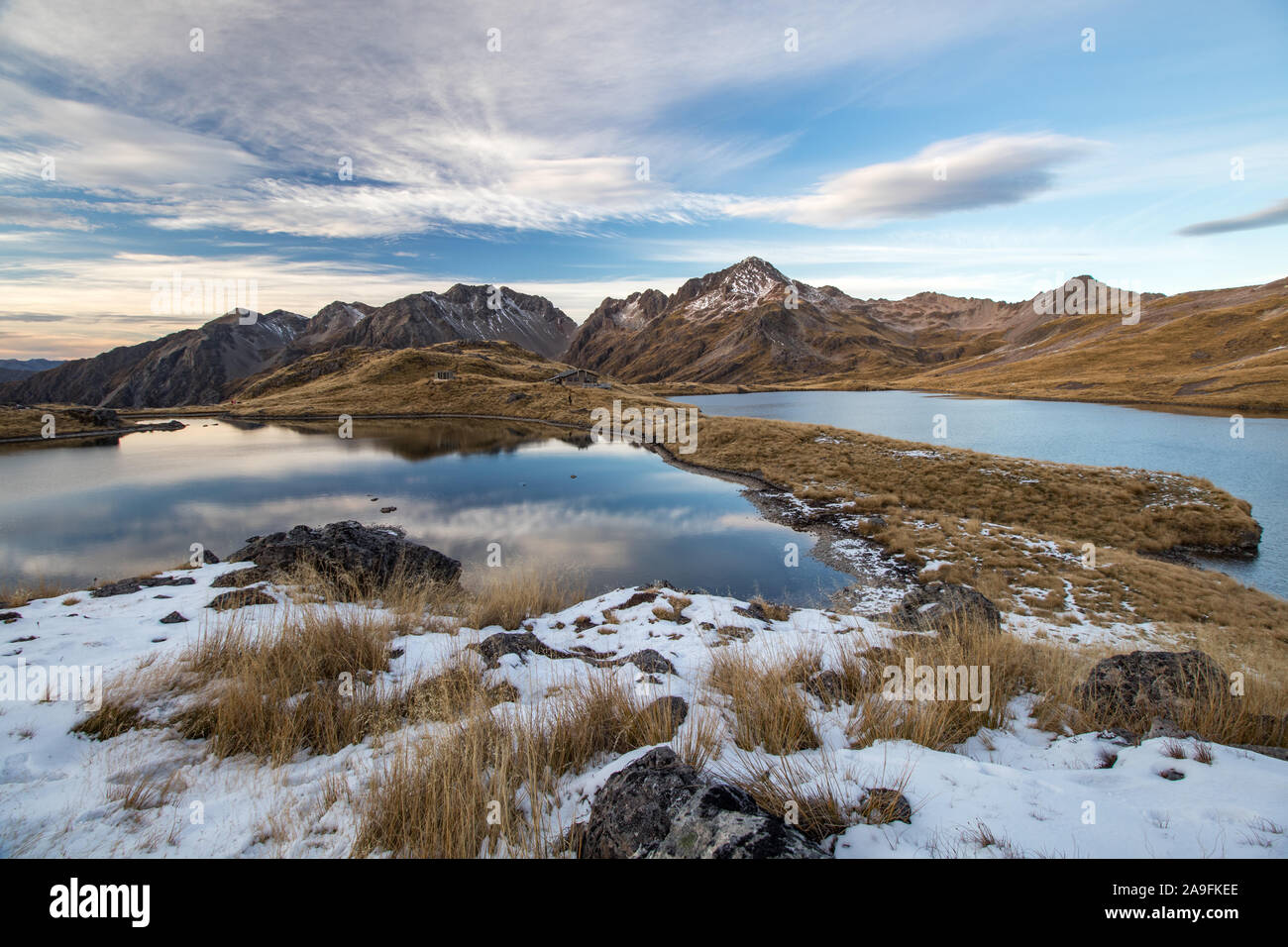 Angelus lakes mirroring fine clouds and blue sky after sunset. Rocky mountains in background with snow, tussock. Angelus mountain hut in the middle Stock Photo