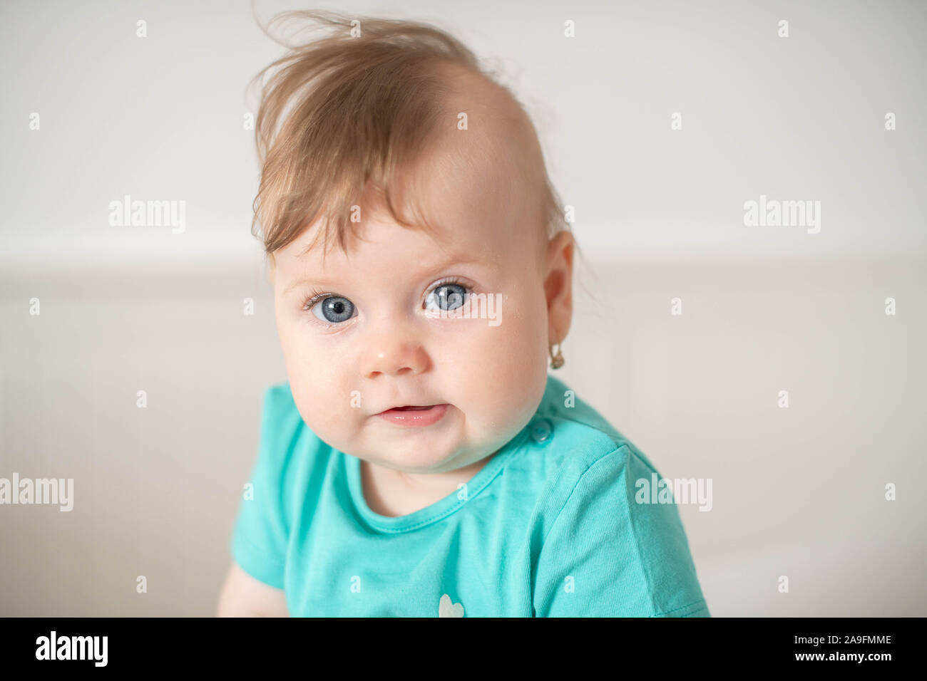 Portrait of adorable Caucasian baby girl with blue eyes, looking at the camera calmly, with curiosity, interactivity or inquisitiveness and sitting Stock Photo