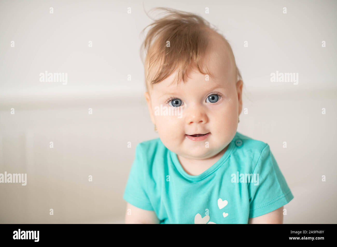 Portrait of adorable Caucasian baby girl with blue eyes, looking at the camera calmly, with curiosity, interactivity or inquisitiveness and sitting Stock Photo